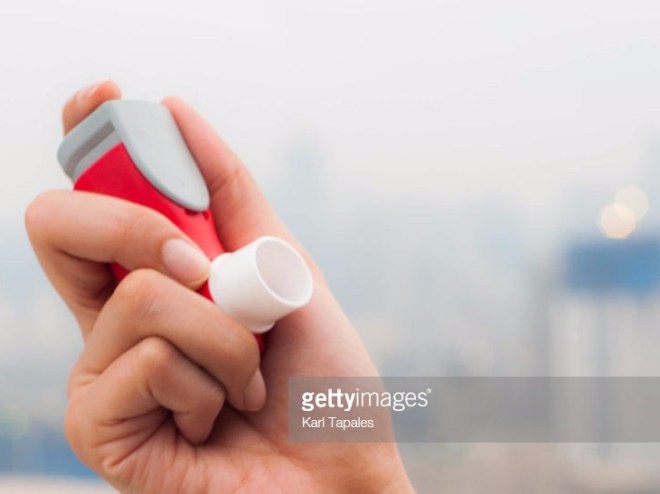 A young woman is using an asthma inhaler outdoor